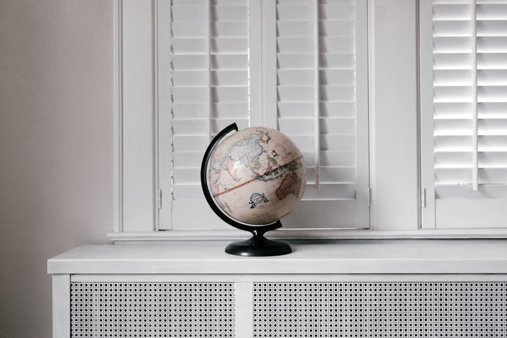 Close-up of modern white window blinds with a silver clock and vase on a shelf below