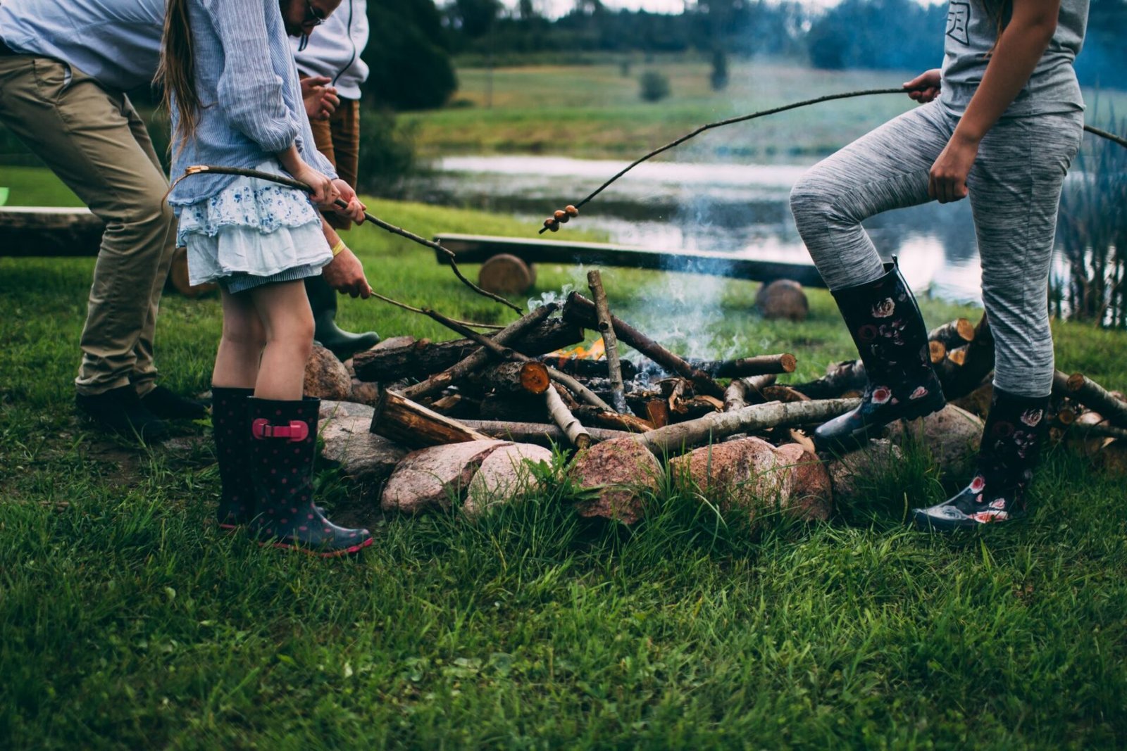 Two people carrying a log near a campfire in a wooded campsite