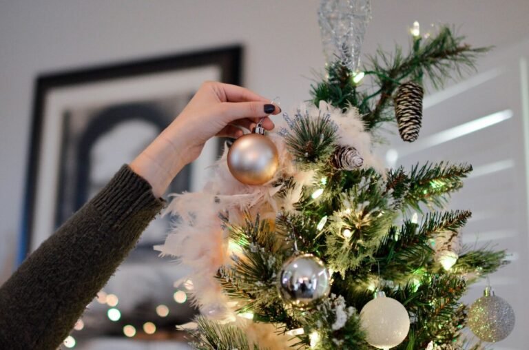 Person placing an ornament on a Christmas tree with pine branches and festive lights