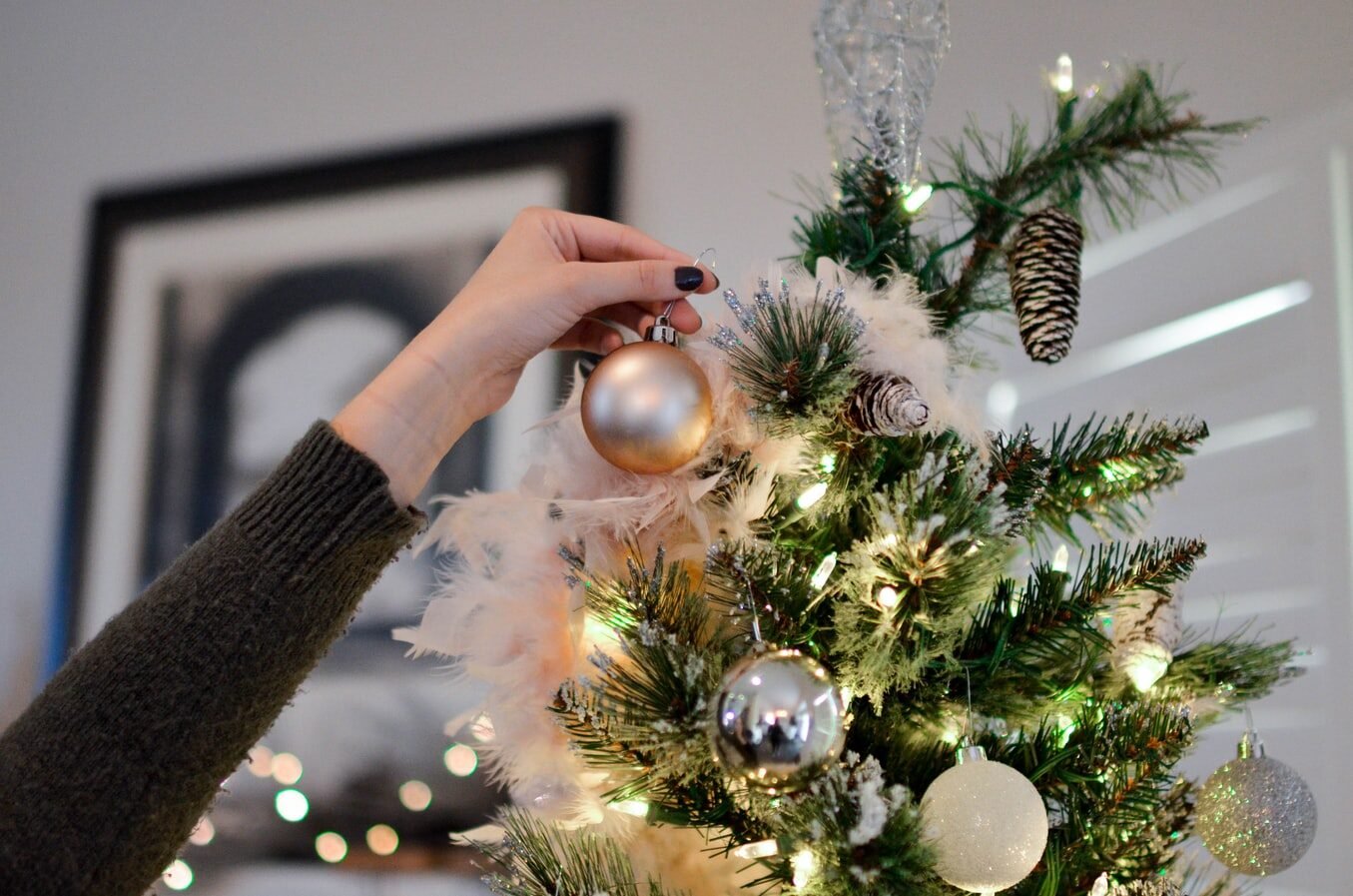 Person placing an ornament on a Christmas tree with pine branches and festive lights