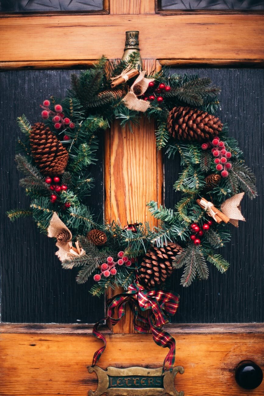 Christmas wreath with pinecones, red berries, and ornaments hanging on a wooden front door