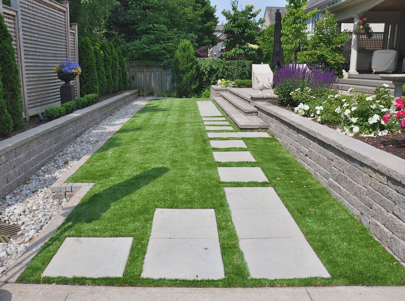 Modern backyard garden with large concrete pavers, green artificial turf, and decorative landscaping